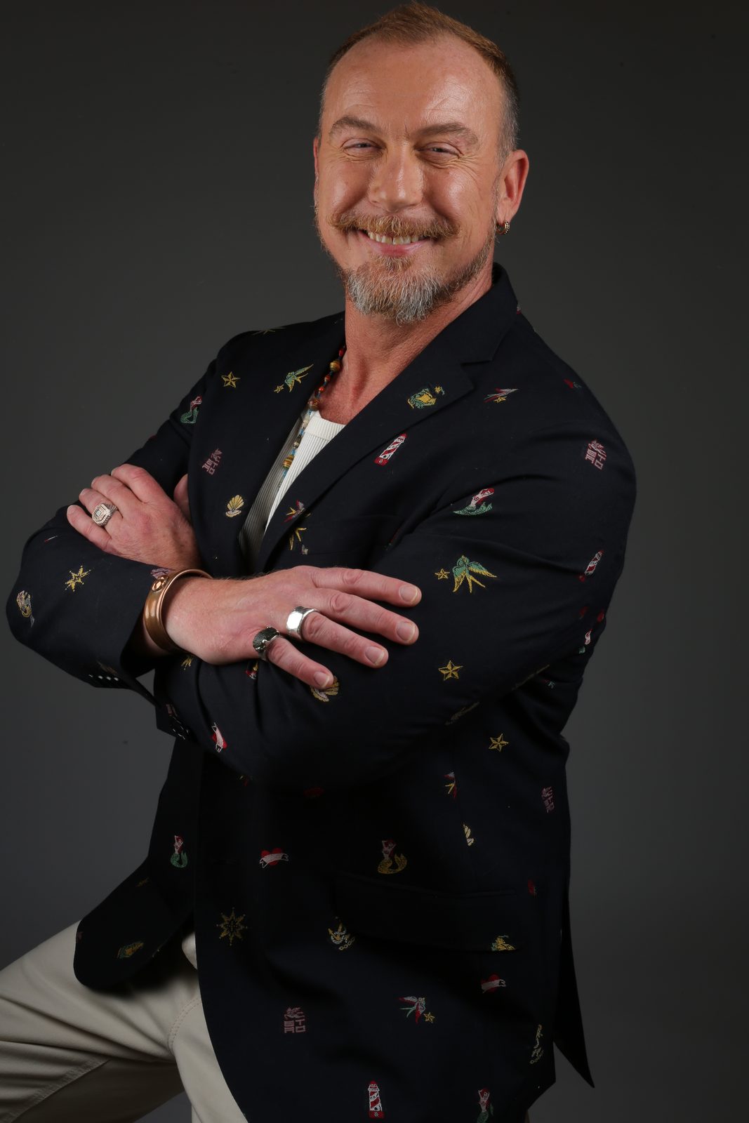 Ross Leslie Nicol smiling with arms crossed, wearing an embroidered navy blazer