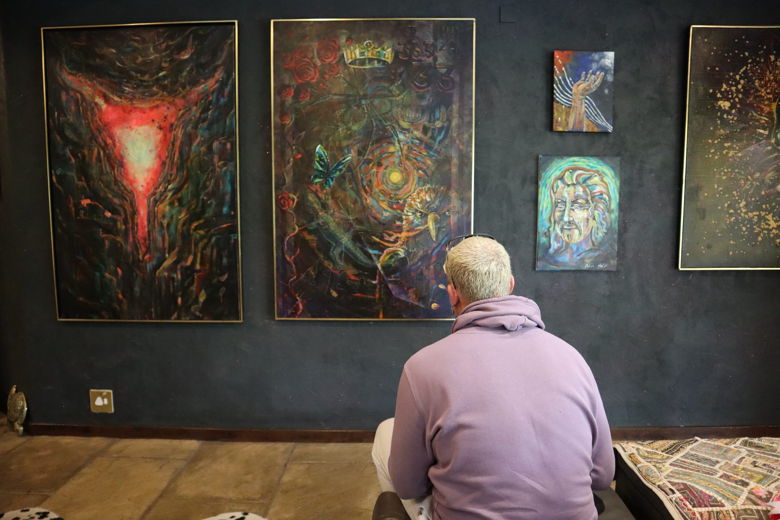 Ross seated in his studio gallery, viewing his large visionary paintings on a dark wall